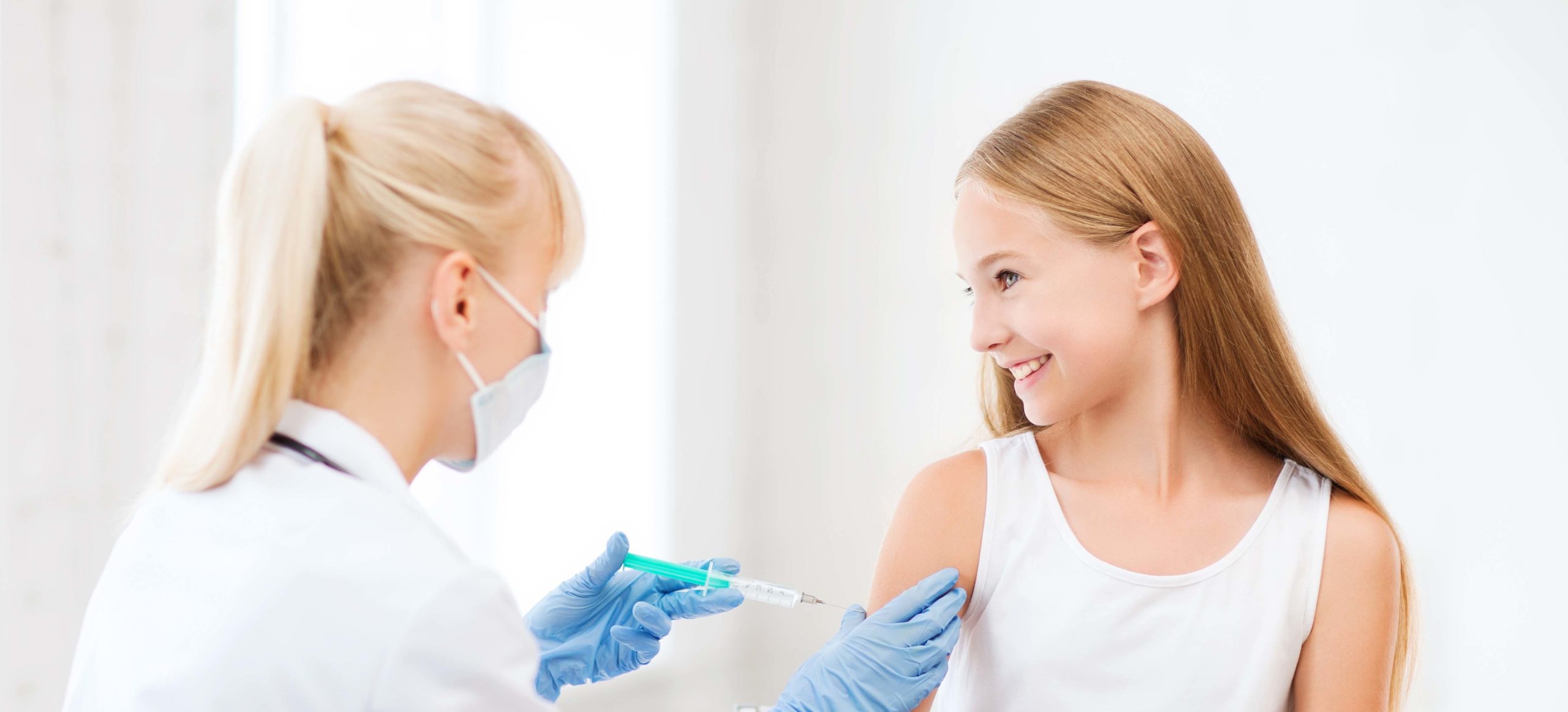 A young girl smiles at a young doctor as she giver her a shot in the arm
