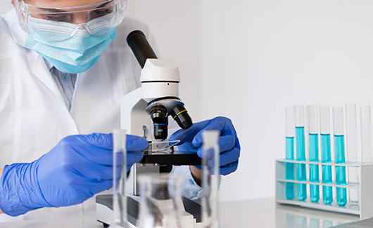 A medical scientist wearing full PPE garb looks at a sample of something through a microscope