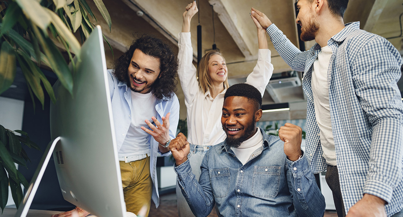 group of overjoyed co-workers celebrating around a computer screen