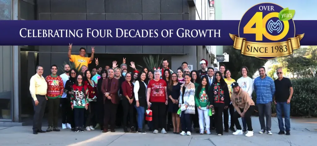 A celebration photo of the entire MMC HR team standing in front of their building posing for the camera, a sticker on the photo reads "celebrating four decades of growth, over 40 years since 1983